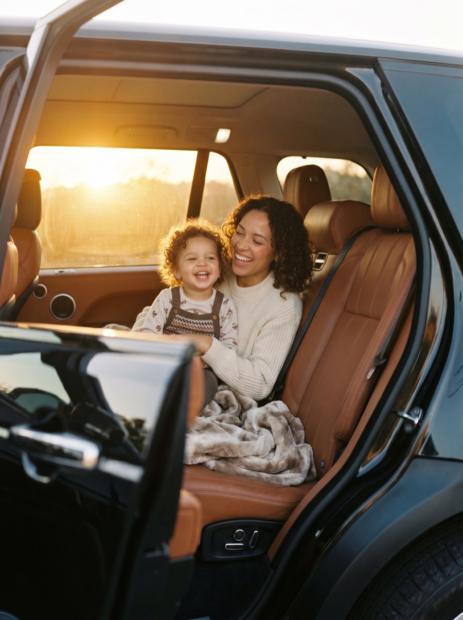 Mother and child seated in the back of a black SUV, daylight